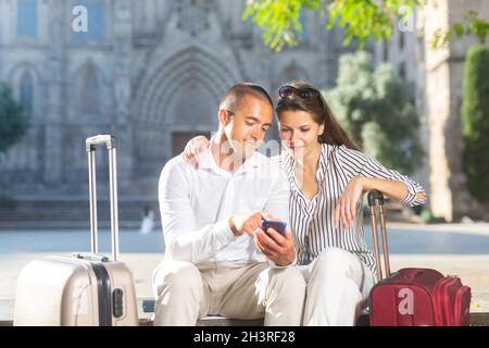 Ein paar Reisende sitzen auf der Bank und buchen die Unterkunft per Telefon Stockfoto