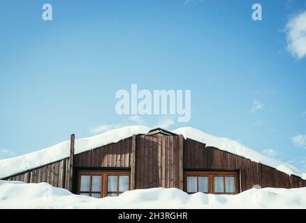 Modernes Holzhaus mit Fenstern und Schnee auf dem Dach, blauer Himmel mit Textraum Stockfoto