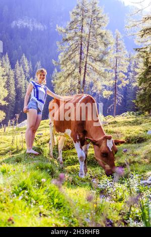 Urlaub auf dem Bauernhof: Junge Frau berührt eine Kuh in einer idyllischen Naturlandschaft Stockfoto