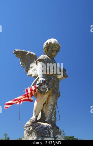 Alte abgenutzte Engelsstatue mit zerfetzter Flagge und blauem Himmel Stockfoto