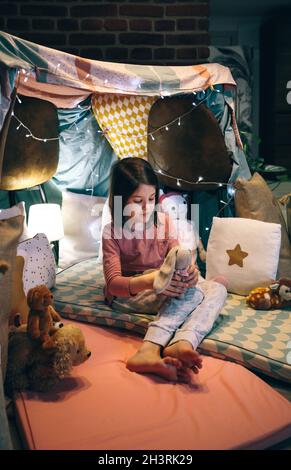 Mädchen im Pyjama spielt mit gefülltem Hase in einem Tipi Stockfoto