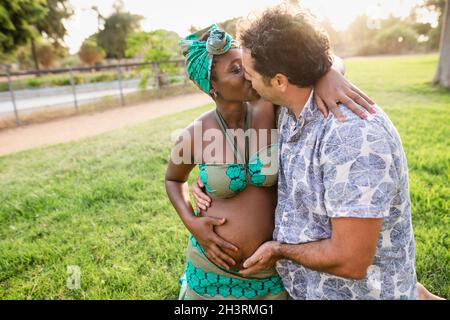 Glückliche afrikanische Schwangeren Frau mit zarten Moment küssen ihren Mann im Park während Sonnenuntergang Zeit Stockfoto