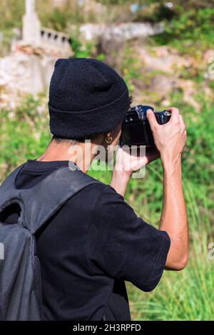 Der junge Fotograf in einem Wollhut macht ein Foto mit seiner Kamera im Wald Stockfoto
