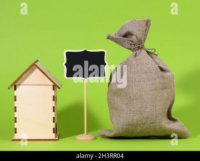 Mini Holzhaus und Kreidezeiger auf grünem Hintergrund. Immobilienkaufkonzept Stockfoto