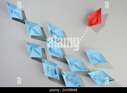 Gruppe von Papierbooten auf grauem Hintergrund. Das Konzept des Denkens über den Tellerrand hinaus, Einzigartigkeit. Stockfoto