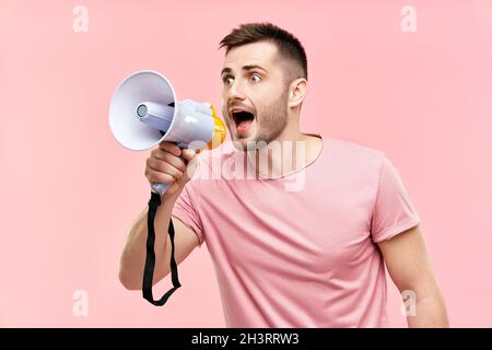 Lustiger junger Mann, der laut schreit und ein Megaphon auf rosa Hintergrund hält Stockfoto