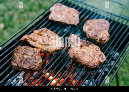 Fünf Steaks auf einem Metallgrill werden auf Kohlen im Grill gebraten. Stockfoto