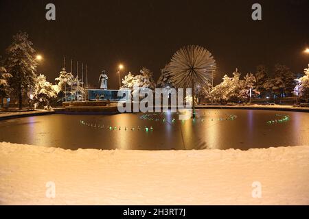 Brunnenbecken und Atatürk-Denkmal im Stadtzentrum von Erzurum bei Nacht unter Schneefall, Langzeitbelichtung. Auf Türkisch als „Havuzbaşı“ bekannt. Stockfoto