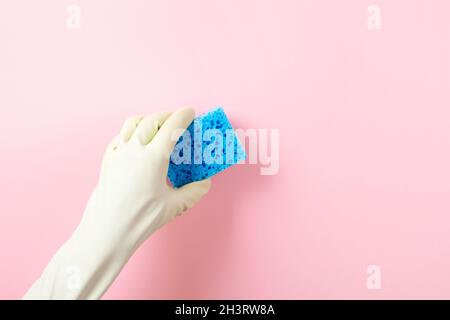 Die Hand in einem grünen Gummihandschuh hält einen blauen Waschschwamm auf rosa Hintergrund Stockfoto