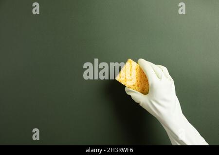 Die Hand in einem grünen Gummihandschuh hält einen gelben Waschschwamm auf grünem Hintergrund Stockfoto