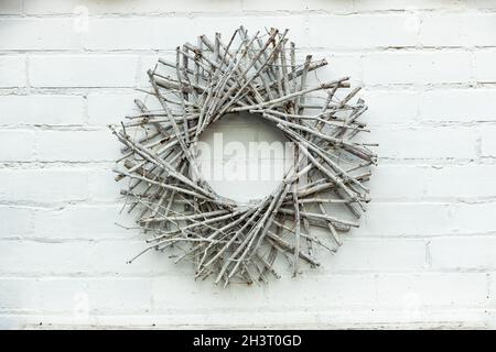 Kreisförmige Dekoration aus Zweigen klebt Äste auf weiß lackierten Ziegelwänden Stockfoto