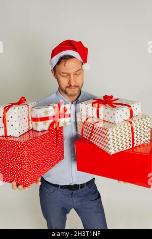 Der brutale Geschäftsmann in Santa hat hält viele Geschenkschachteln in seinen Händen. Studio auf grauem Hintergrund aufgenommen, Weihnachtskonzept. Stockfoto