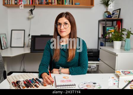 Porträt einer Illustratorin, die in ihrem Atelier die Kamera anschaut Stockfoto