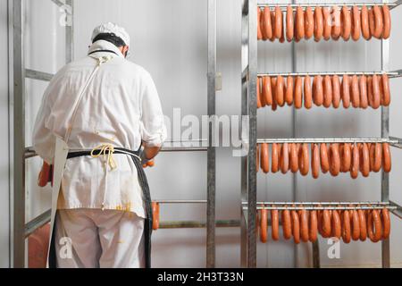 Der Arbeiter hängt Rohwürste an Regalen im Lagerraum der Fleischverarbeitungsfabrik Stockfoto