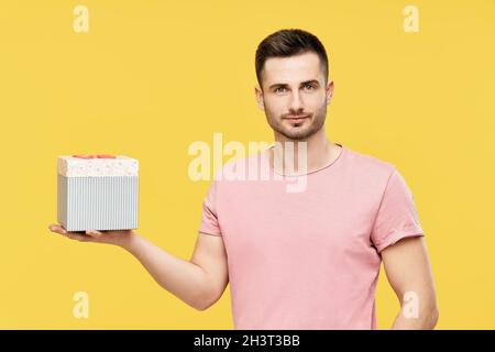 Hübscher junger Mann mit Geschenkbox auf gelbem Studiohintergrund Stockfoto