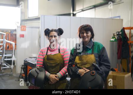 Porträt zweier Schweißer, die Schweißmasken in den Händen halten und sich auf harte Arbeit in einer Fabrik vorbereiten Stockfoto