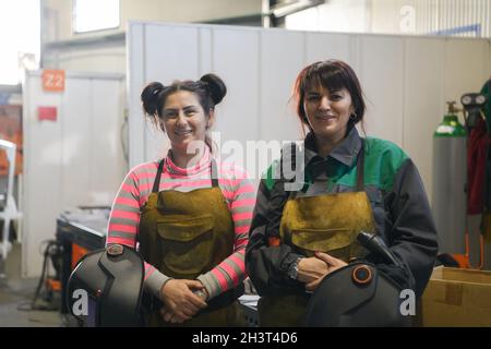 Porträt zweier Schweißer, die Schweißmasken in den Händen halten und sich auf harte Arbeit in einer Fabrik vorbereiten Stockfoto