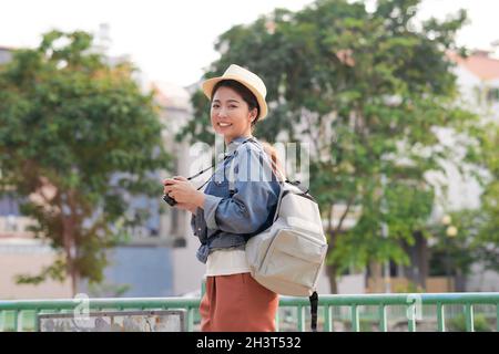 Junge schöne asiatische Rucksack Reisende Frau mit digitalen Kompaktkamera und Lächeln, Blick auf Copy Space Stockfoto