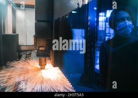 Funken fliegen aus dem Maschinenkopf für Metall verarbeitende Lasermetalle auf metallurgischem Werkshintergrund. Fertigung von Fertigteilen für Stockfoto