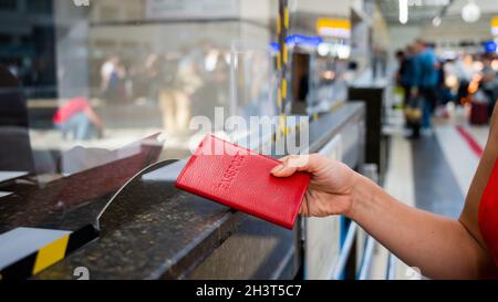 Gesichtslose Frau, die ihren Pass am Check-in-Schalter am Flughafen ausgibt. Stockfoto
