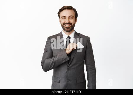 Gutaussehender bärtiger Firmenmann legte Kreditkarte in die Tasche, lächelnd zufrieden, Konzept von Geld und Investitionen, weißer Hintergrund Stockfoto