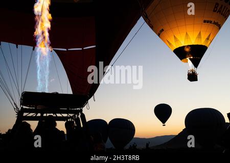 GOREME, TÜRKEI - 3. AUGUST 2021: Silhouetten von Touristen und Reisenden am frühen Morgen, die die Heißluftballons beim Start beobachten Stockfoto