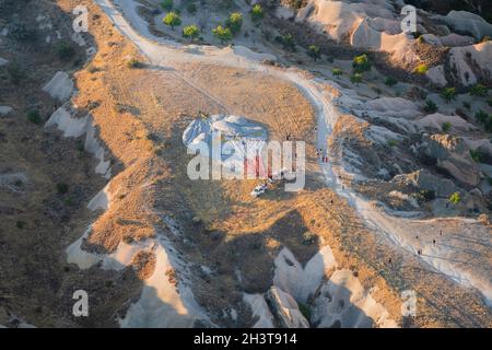 GOREME, TÜRKEI - 3. AUGUST 2021: Draufsicht auf den entflachten Heißluftballon aus der Luft nach dem Morgenflug mit Touristen, die sich um ihn herum versammelten Stockfoto