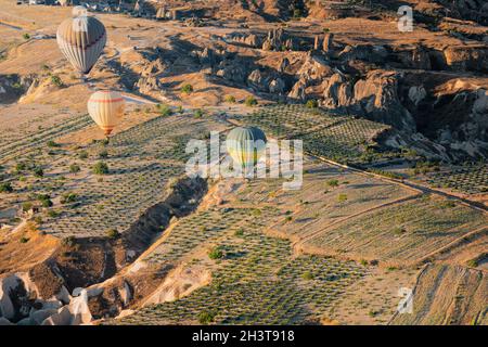 GOREME, TÜRKEI - 3. AUGUST 2021: Farbenfrohe Heißluftballons fliegen im Morgenlicht sehr nahe am Boden über das Kappadokien-Tal Stockfoto