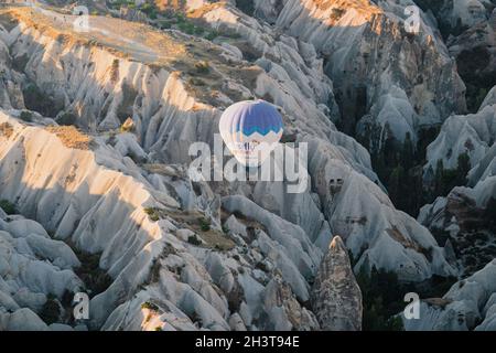 GOREME, TÜRKEI - 3. AUGUST 2021: Ein einsamer, farbenfroher Heißluftballon, der im Morgenlicht sehr nahe am Boden über dem Kappadokien-Tal fliegt Stockfoto