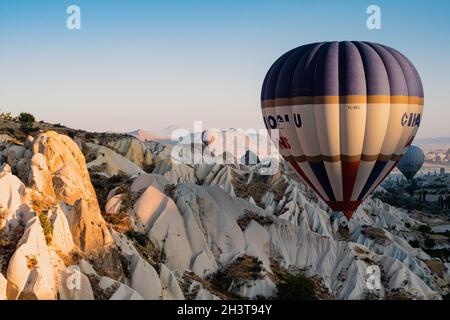 GOREME, TÜRKEI - 3. AUGUST 2021: Farbenfrohe Heißluftballons fliegen im Morgenlicht sehr nahe am Boden über das Kappadokien-Tal Stockfoto