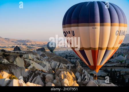 GOREME, TÜRKEI - 3. AUGUST 2021: Farbenfrohe Heißluftballons fliegen im Morgenlicht sehr nahe am Boden über das Kappadokien-Tal Stockfoto