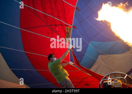 GOREME, TÜRKEI - 3. AUGUST 2021: Die Menschen arbeiten hart daran, auf dem Boden einen Heißluftballon mit der warmen Luft aus der Brennerflamme aufzublasen, damit die Tour Stockfoto