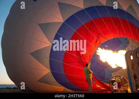 GOREME, TÜRKEI - 3. AUGUST 2021: Die Menschen arbeiten hart daran, auf dem Boden einen Heißluftballon mit der warmen Luft aus der Brennerflamme aufzublasen, damit die Tour Stockfoto