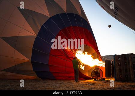 GOREME, TÜRKEI - 3. AUGUST 2021: Die Menschen arbeiten hart daran, auf dem Boden einen Heißluftballon mit der warmen Luft aus der Brennerflamme aufzublasen, damit die Tour Stockfoto