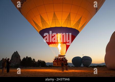 GOREME, TÜRKEI - 3. AUGUST 2021: Die Leute stellen sich zum Abheben eines Heißluftballonkorbes voller Touristen auf, während der Kapitän die Brennerflamme anfeuert Stockfoto