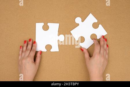 Zwei leere papierweiße Puzzleteile in weiblichen Händen, Puzzle verbunden, brauner Hintergrund Stockfoto