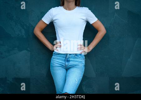 Weißes Mockup-T-Shirt in Druckdesign. Junge, stylische Frau in blanko weißem T-Shirt und blauer Jeans auf grauem Hintergrund Stockfoto