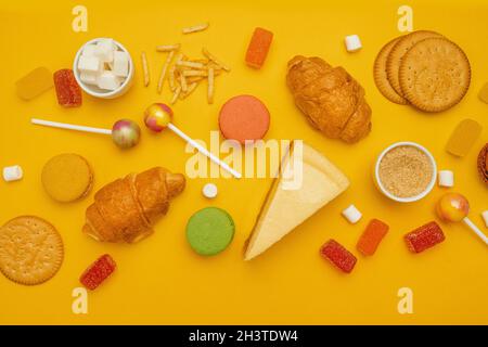 Französisches Croissant, Bonbons auf einem Stock, Gelee-Bonbons, Marschmalchen, Kekse und Makronen auf gelbem, hellem Hintergrund. Ungesunde Lebensmittel auf farbigem Rücken Stockfoto