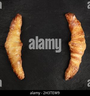 Zwei Croissants auf schwarzem Hintergrund, von oben geschossen, bilden einen Rahmen Stockfoto