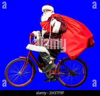 Fröhlicher Weihnachtsmann in einem Neujahrshut und roter Kleidung fährt mit einer Geschenktüte auf dem Fahrrad. Isolieren. Frohes neues Jahr 2022. Frohe Weihnachten. Konz Stockfoto