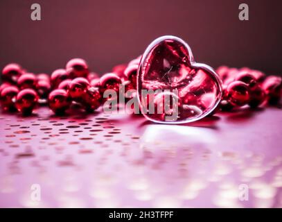 Leuchtendes transparentes Herz und eine Gruppe roter Perlen. Perfekte Valentinstag Grußkarte Hintergrund. Horizontales Bild in rosa t Stockfoto