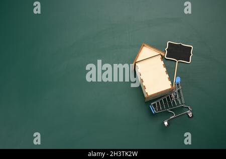 Holzhaus in Miniatur-Metall-Warenkorb auf grünem Hintergrund Stockfoto