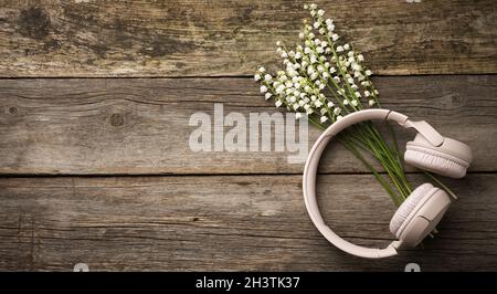 Beigefarbene kabellose Kopfhörer auf einem Holztisch, neben einem Bouquet aus weißen Lilien des Tals Stockfoto
