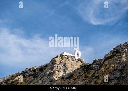 Kleine alte Kapelle, weiße Wände und Glockenturm, orthodoxe griechische Kirche auf dem felsigen Hügel, blauer Himmel Hintergrund. Serifos Island, Griechenland Stockfoto