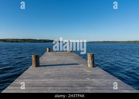 Hölzerne Promenade, die unter wolkenlosem, blauem Himmel in das dunkelblaue Wasser eines Fjords führt Stockfoto