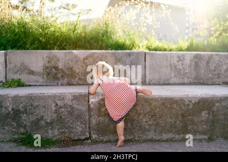 Kleines Mädchen in einem Kleid klettert hohe Steintreppen im Park Stockfoto