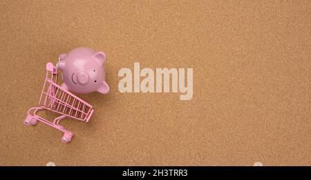 Rosa Warenkorb und Keramik Sparschwein auf braunem Hintergrund, Banner. Shopping Sparkonzept, Verkauf Stockfoto