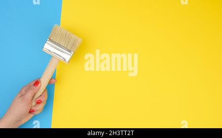 Weibliche Hand halten neuen Pinsel mit Holzgriff auf einem gelben Hintergrund Stockfoto