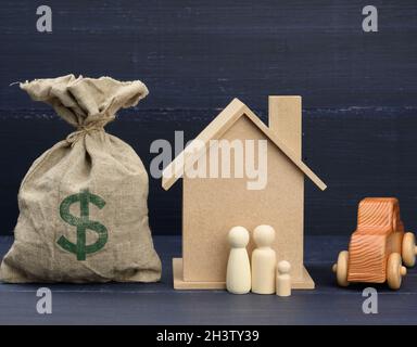 Leinentasche voller Geld und ein Holzhaus auf blauem Hintergrund. Das Konzept des Immobilienkaufs Stockfoto