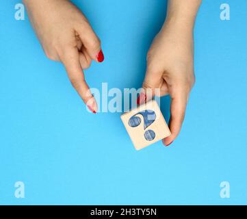 Weibliche Hand, die einen Holzwürfel mit einem Fragezeichen auf blauem Hintergrund hält, das Konzept der Antworten und Fragen Stockfoto